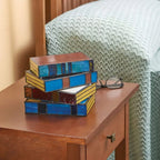 Vintage stained glass table lamp shaped like a stack of colorful books on a wooden bedside table.